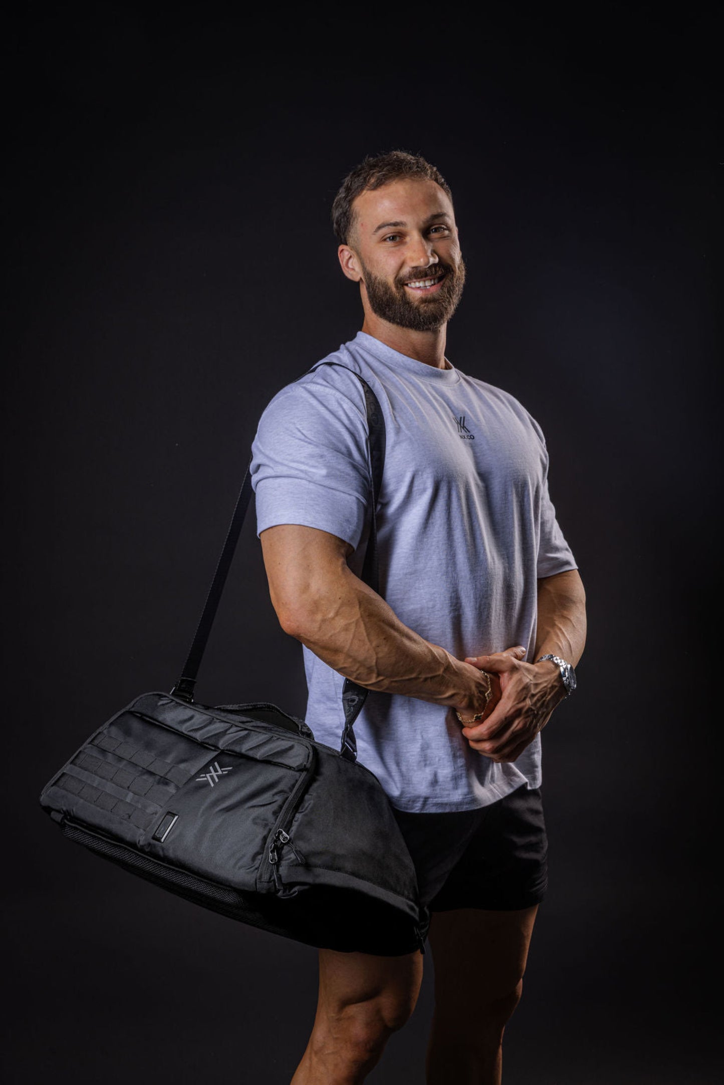 Man holding a black gym bag against a dark background