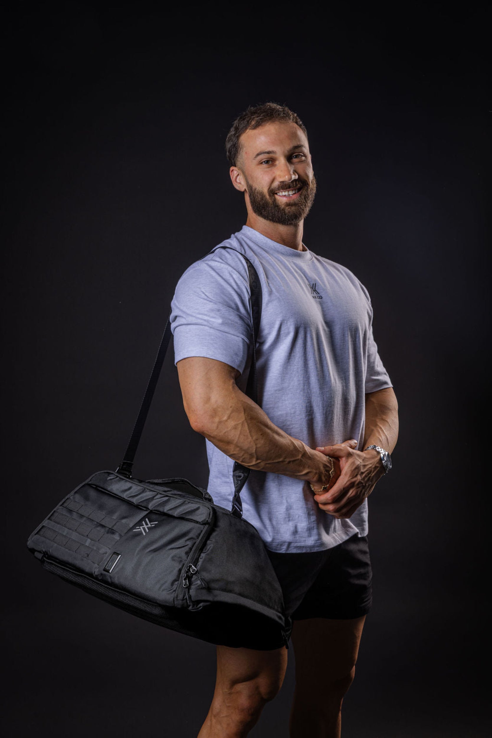 Man holding a black gym bag against a dark background